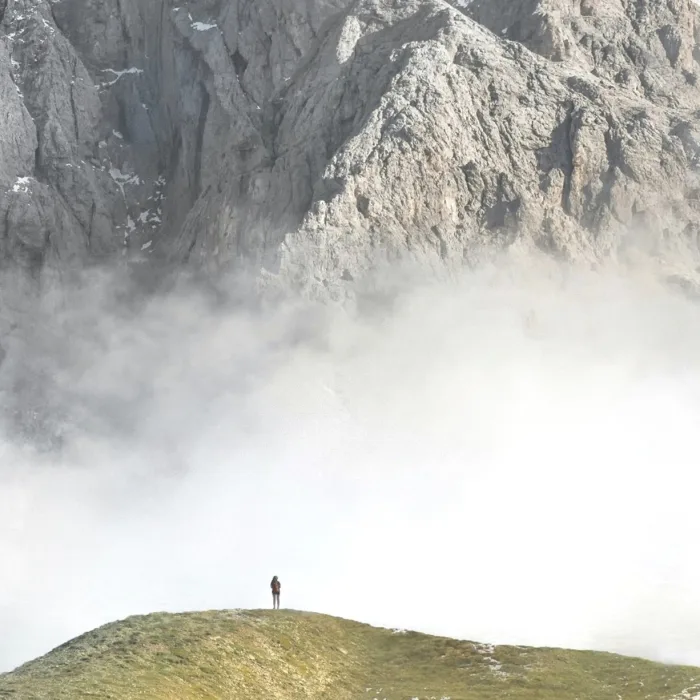 Randonneuse seule sur une crête, face à une paroi de montagne dans la brume