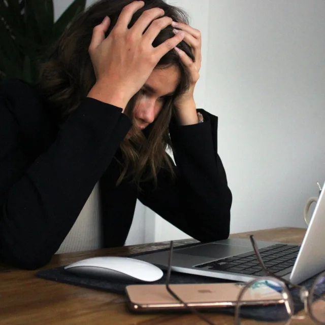 Personne en veste, tête entre les mains devant son ordinateur portable