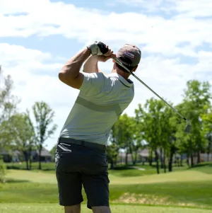Golfer seen from behind, mid-swing on a tree-lined course