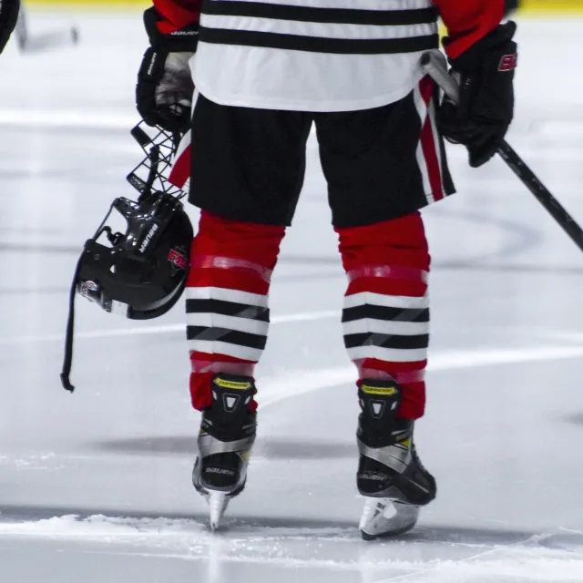 Hockey player seen from behind, skates and pads, helmet in hand on the ice