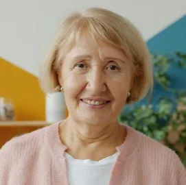 Smiling older woman in a pink cardigan, in a brightly coloured room