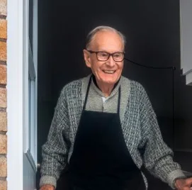 Smiling older man in an apron, standing in his doorway