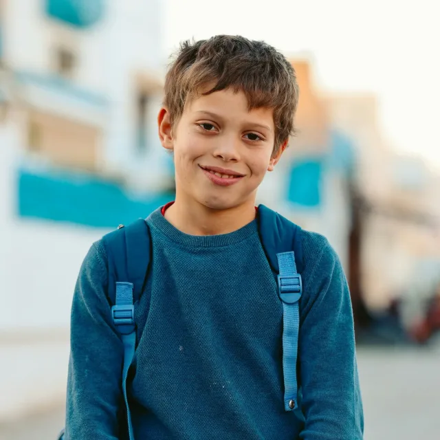 Smiling boy with a blue backpack on his shoulders, out in the street